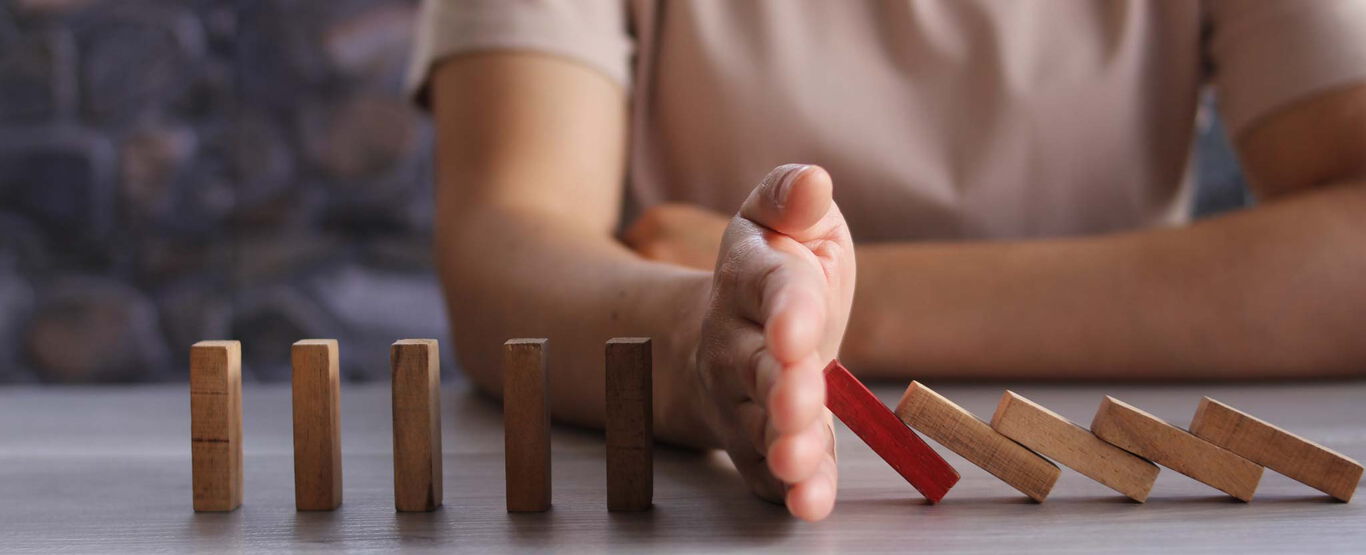 hand-stoppt-reihe-umfallender-Holzsteine-und-schuetzt-damit-die-restlichen-steine